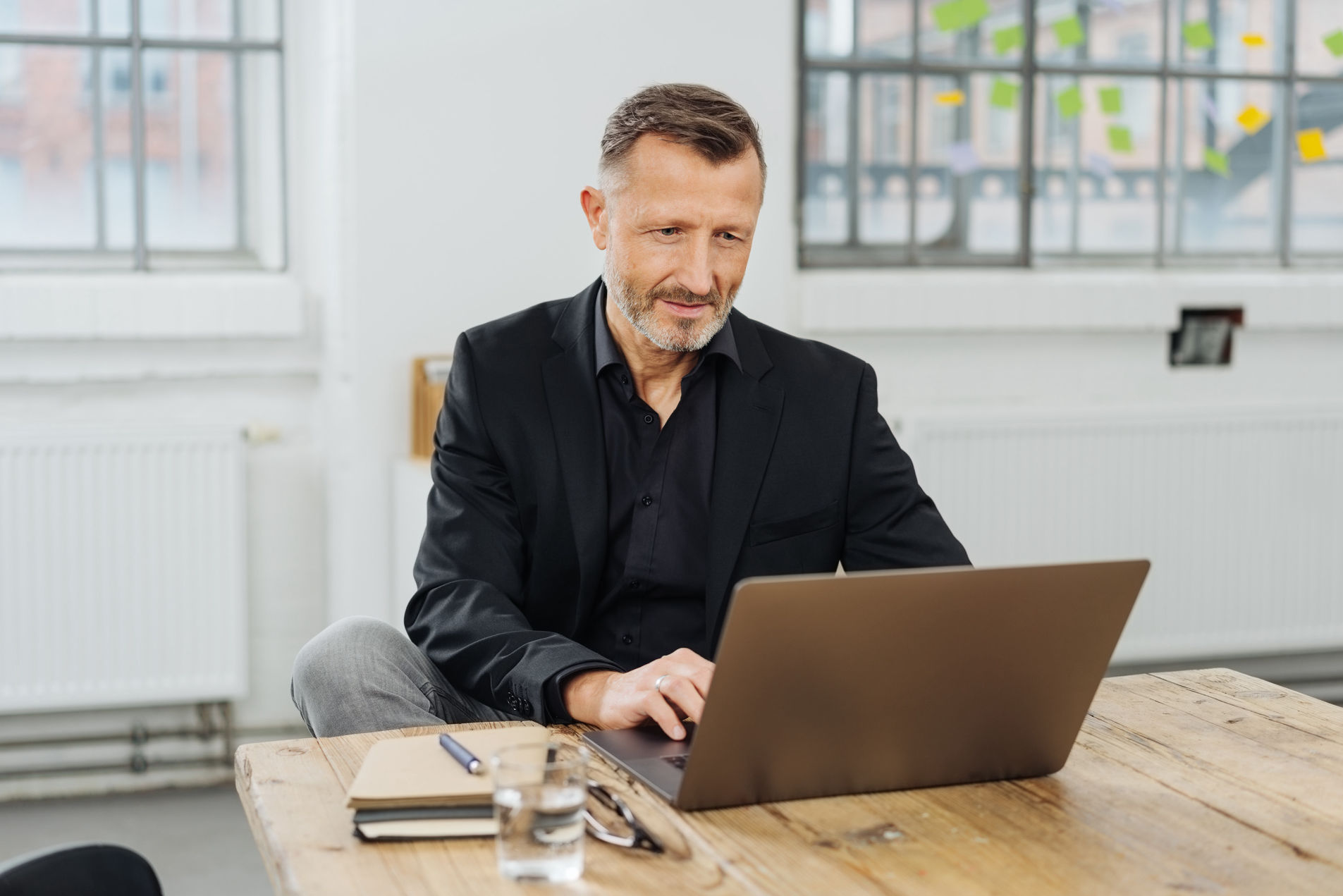 Mann mit Bart, der lächeln und zufrieden vor seinem Laptop sitzt