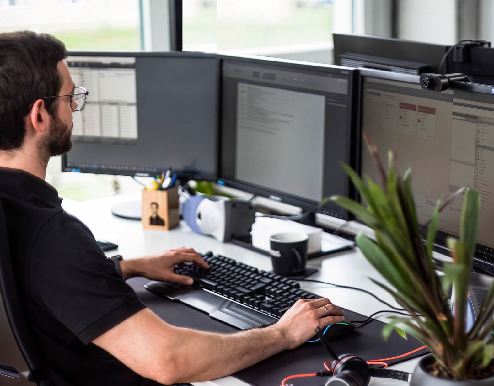 Unser IT Administrator sitzt vor drei Bildschirmen, den Blick konzentriert darauf und den Finger auf der Tastatur.